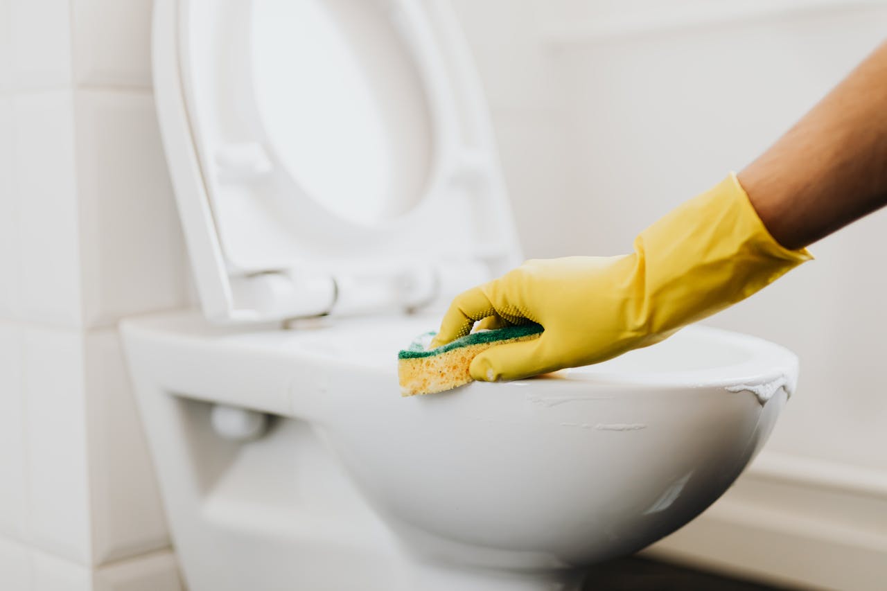 contact-img A close-up of a hand in a yellow glove cleaning a toilet with a sponge, promoting hygiene.
